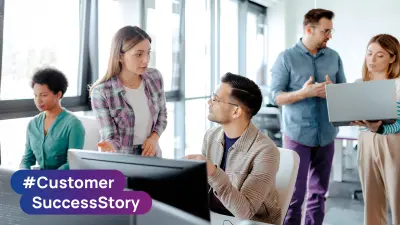 Team members collaborating around computer workstations in an office with #Customer SuccessStory branding.