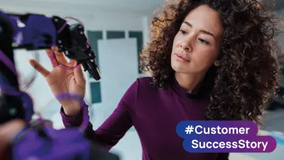 Person inspecting a robotic device in a laboratory environment with #Customer SuccessStory branding.