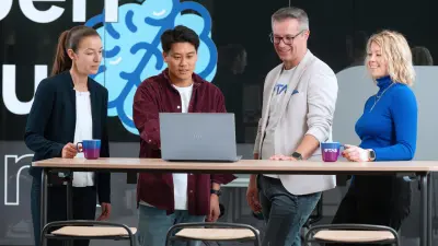 多様な4人の専門家がスタンディングデスクで協働し、ノートパソコンに向かっている。