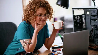Woman holding a cup and looking at a laptop