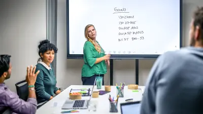 Team sits in a meeting and a woman stands at the front and outlines the goals