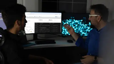 Two men sit in front of a PC and discuss the content