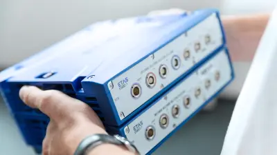 Close-up of a person holding two stacked ETAS ES882.1 hardware devices with visible connection ports, highlighting precision equipment for calibration and testing.
